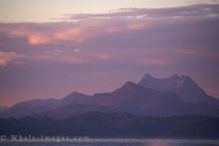 The mountain peaks still display a small amount of snow as the pinkish hues from the sunset alter the color of the world around Northern Vancouver Island in British Columbia, Canada.